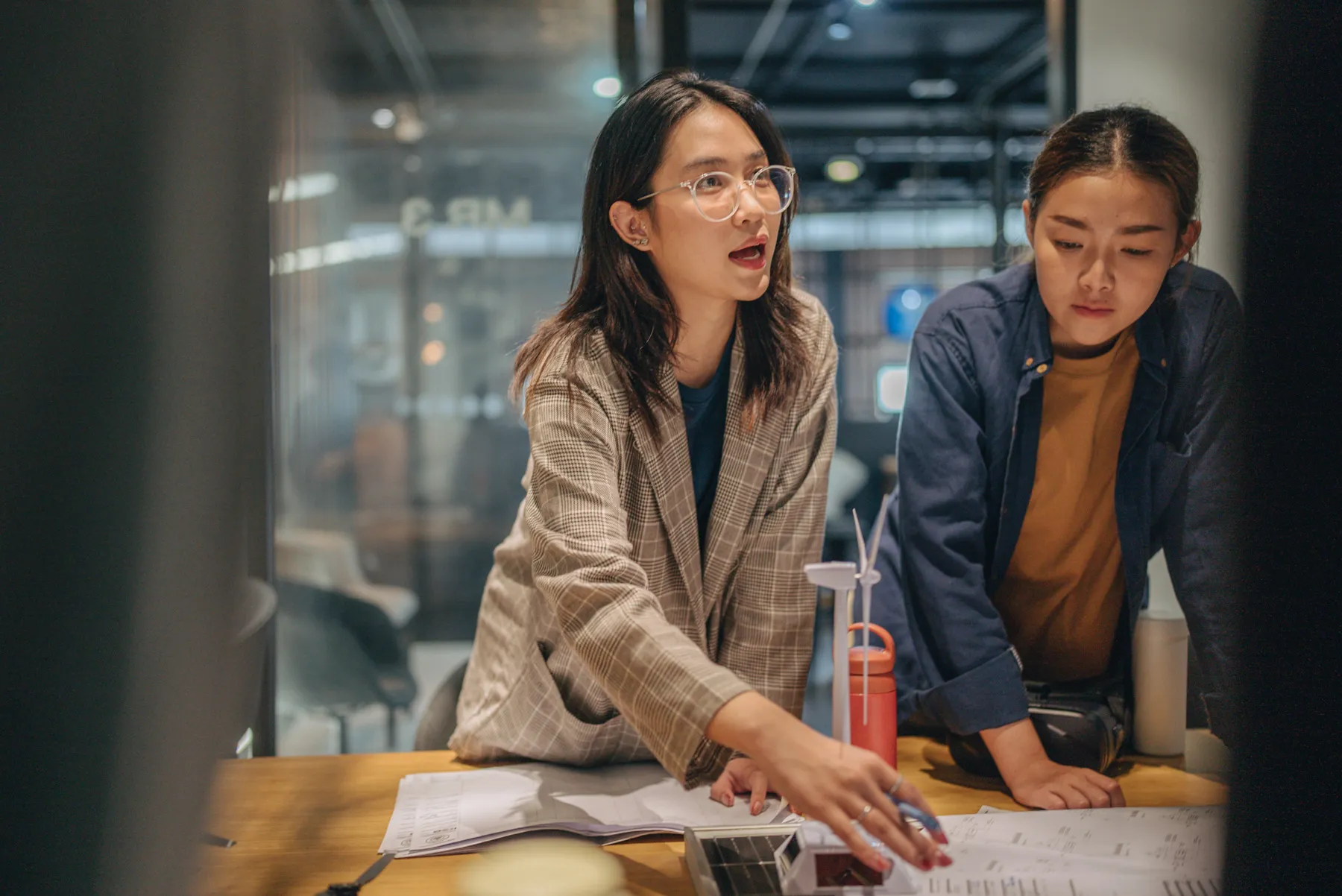 Two women reviewing notes on a table during a meeting.